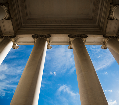 Ground up view of huge white columns of a law building with blue skies