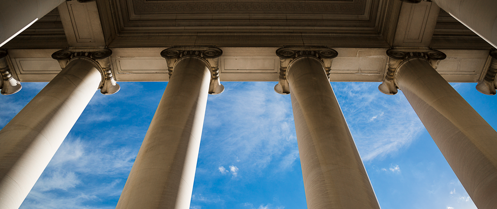 Ground up view of huge white columns of a law building with blue skies